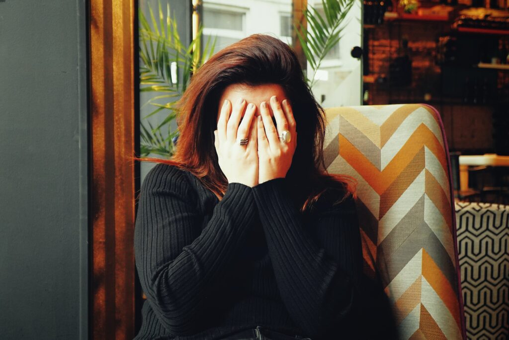 a brunette woman holding her hands over her face in pain as if she has a headache or migraine